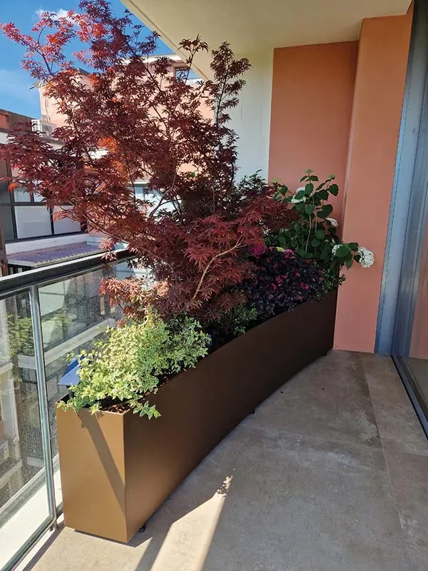 Fioriera lunga in corten con un acero rosso e piante ricadenti sul balcone di un palazzo