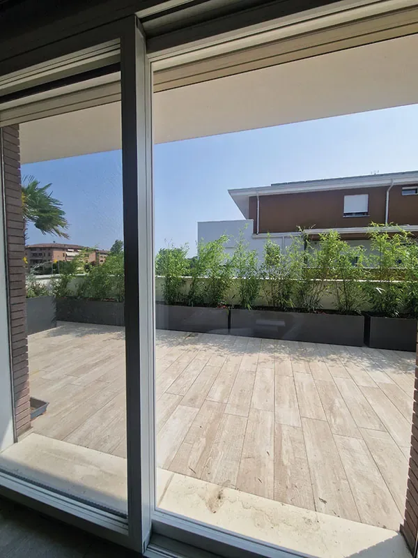 Terrazzo con pavimento effetto legno e fioriere di bambù lungo il parapetto, visto dalla porta finestra