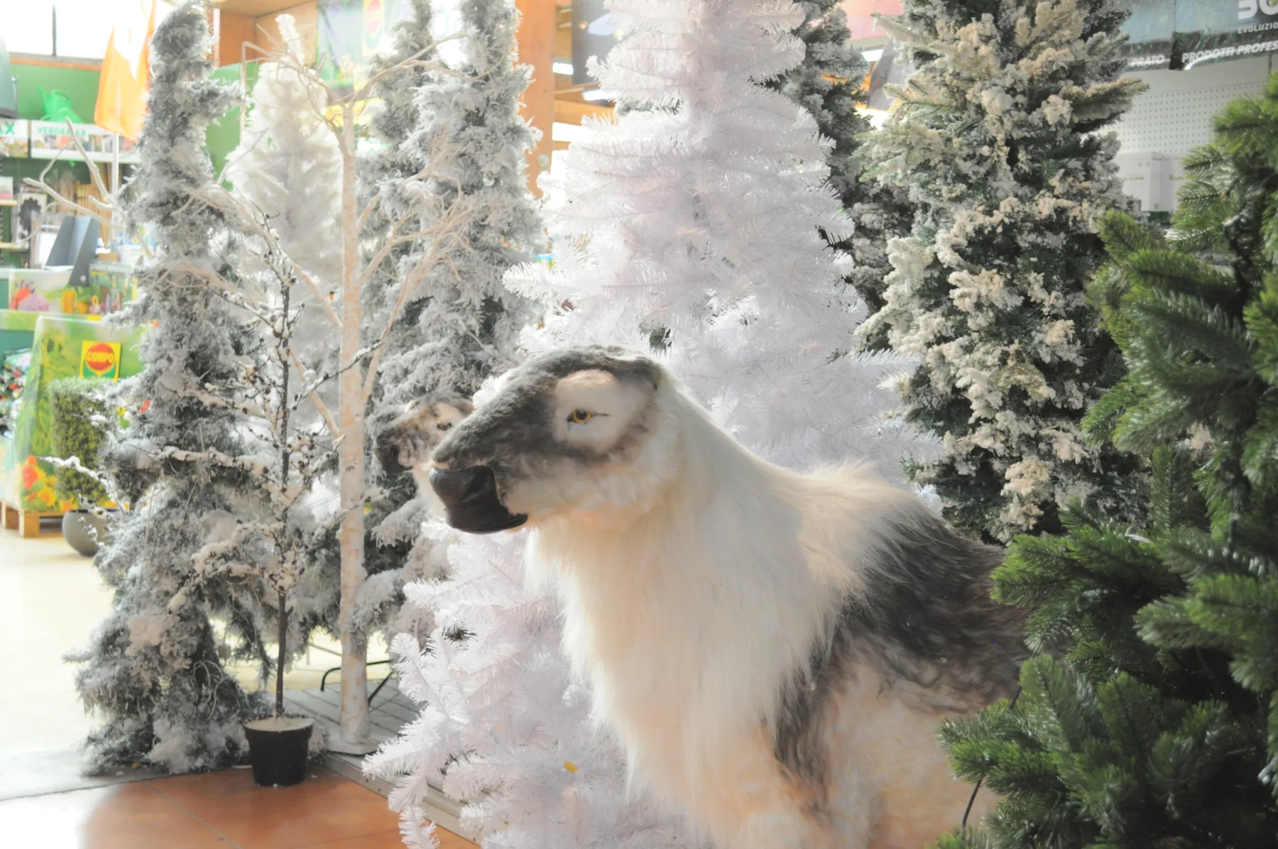 Una renna di peluche bianca e grigia fra abeti sintetici innevati