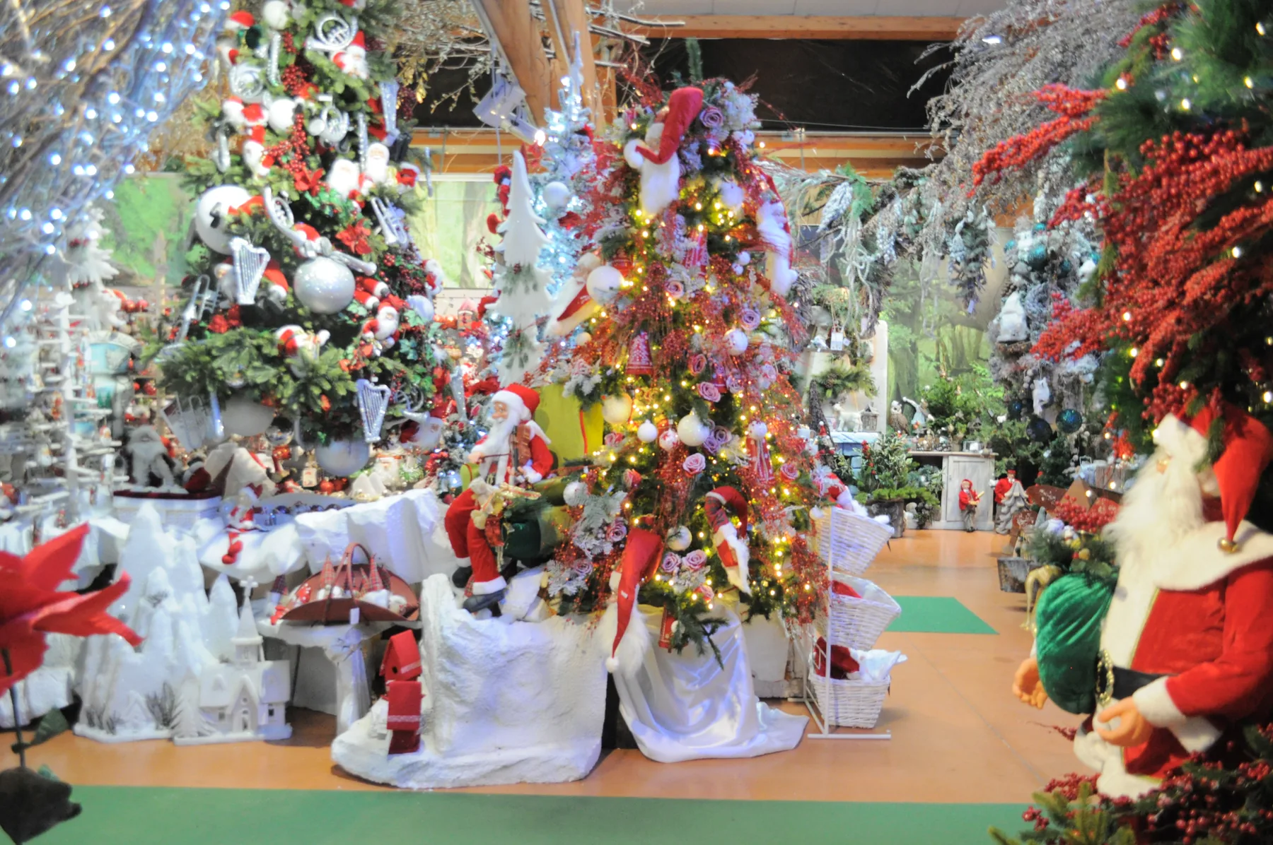 Albero addobbato di rosso e bianco fra cuscini bianchi, con pupazzi di Babbo Natale e altri alberi decorati