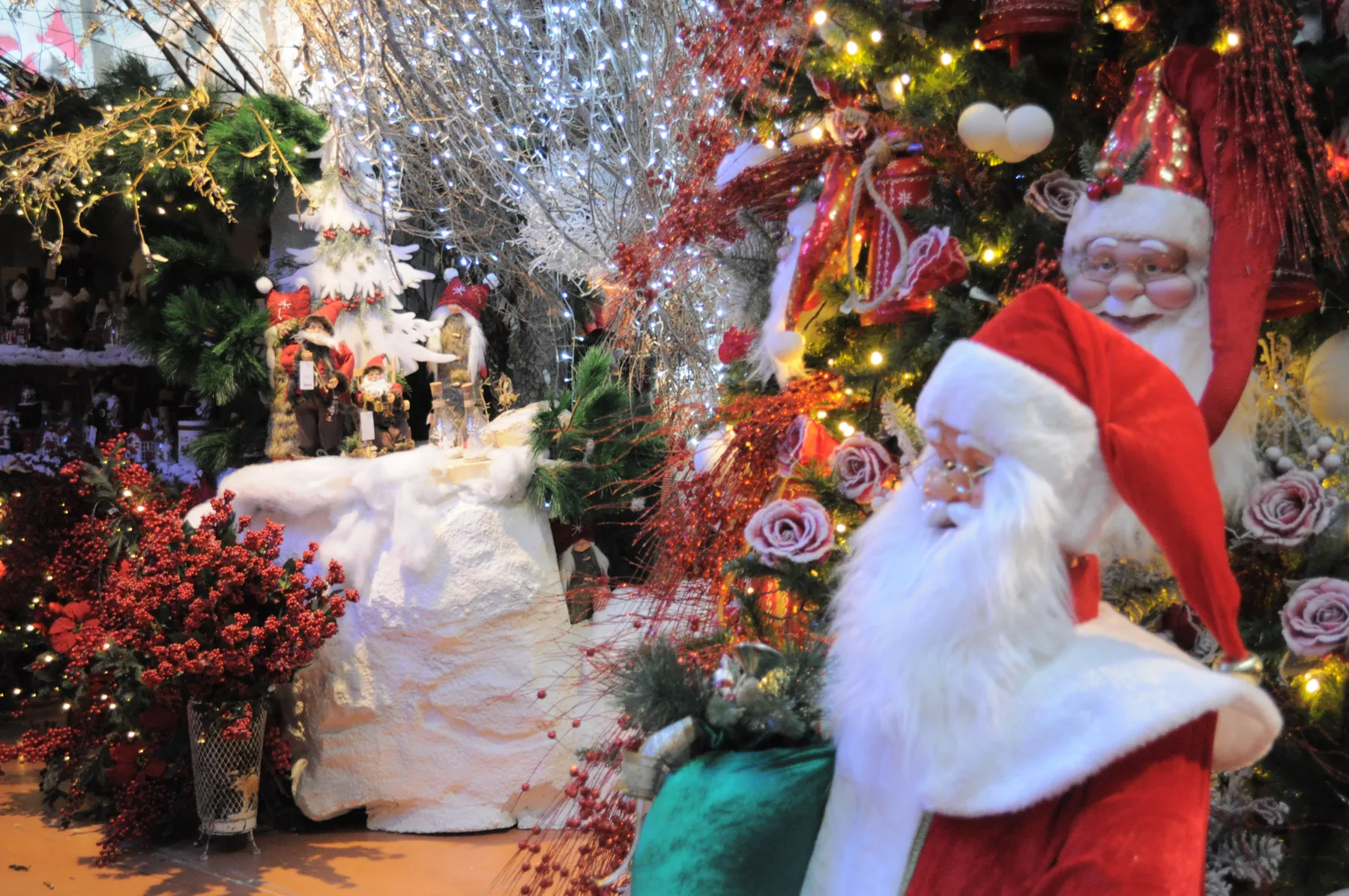 Pupazzo di Babbo Natale con il cappello rosso fra abeti addobbati e cuscini bianchi