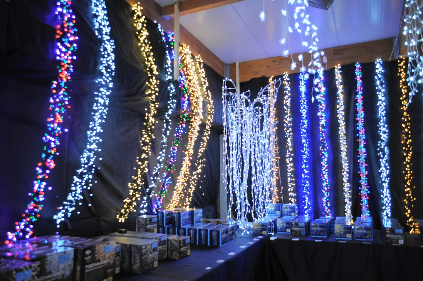 Tende di luci blu, bianche e dorate appese in un reparto buio, sopra le scatole delle luminarie