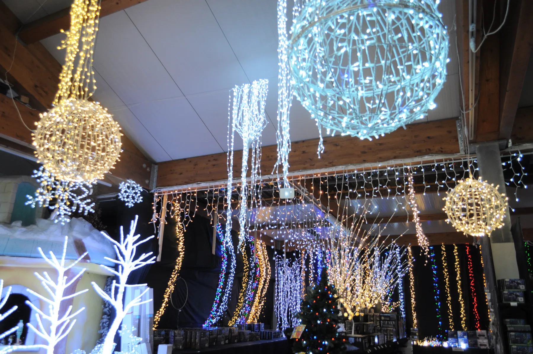 Grandi sfere di luce azzurre e dorate appese al soffitto, con tende luminose e alberi bianchi