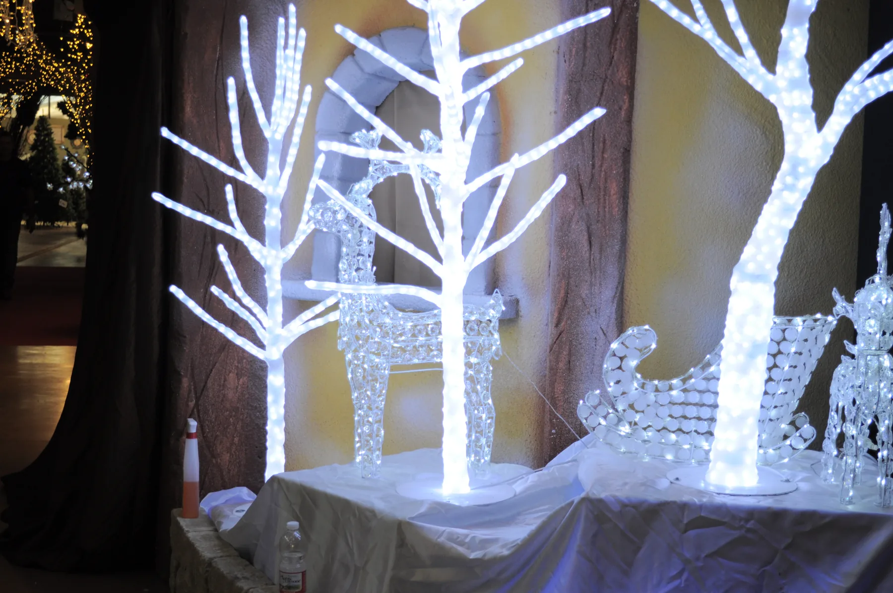 Alberi di luce bianca e una renna luminosa trasparente su un piano coperto di bianco