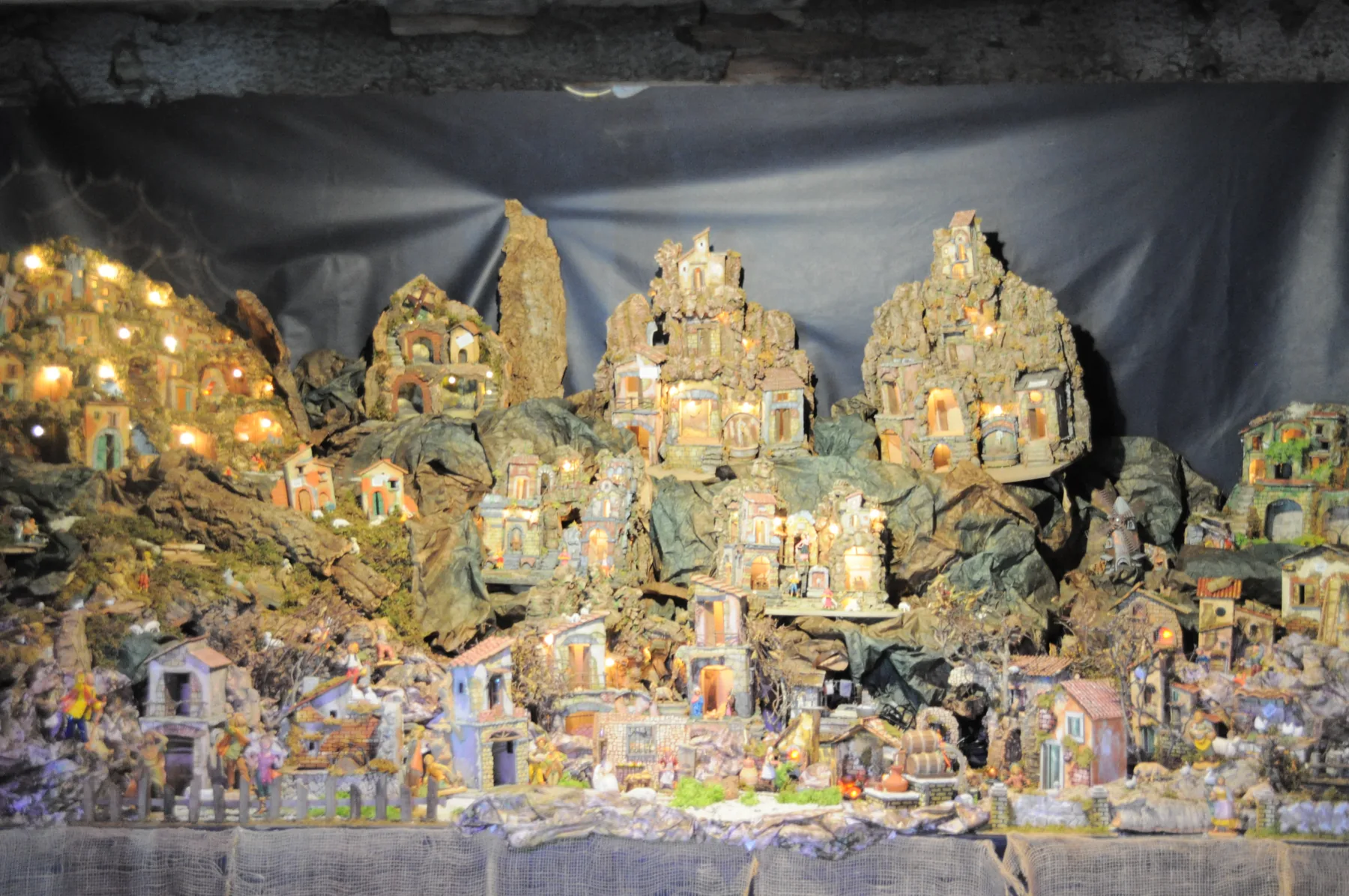 Grande presepe napoletano con borghi di case in pietra illuminate, grotte e statuine