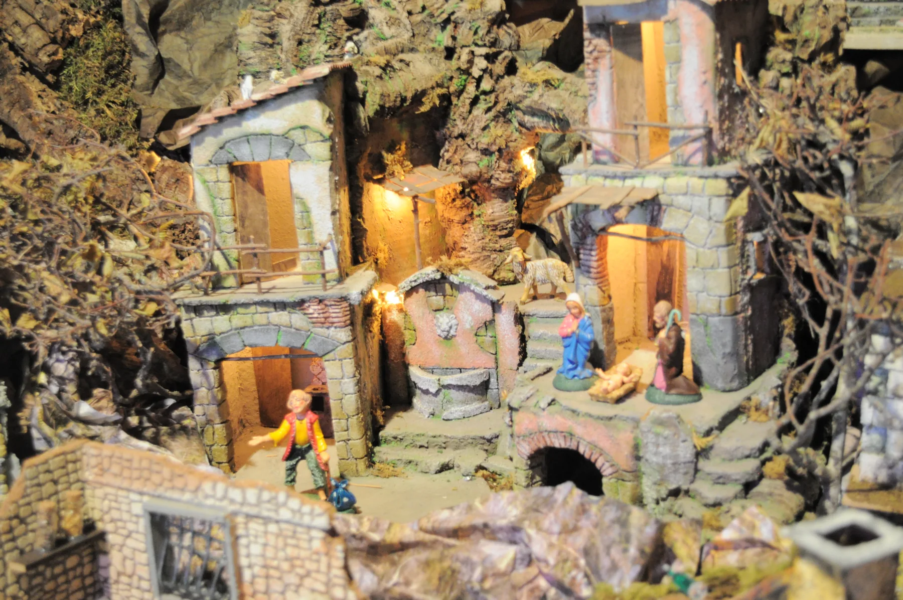 Presepe con case di pietra illuminate, la natività nella grotta e un pastore sulla strada