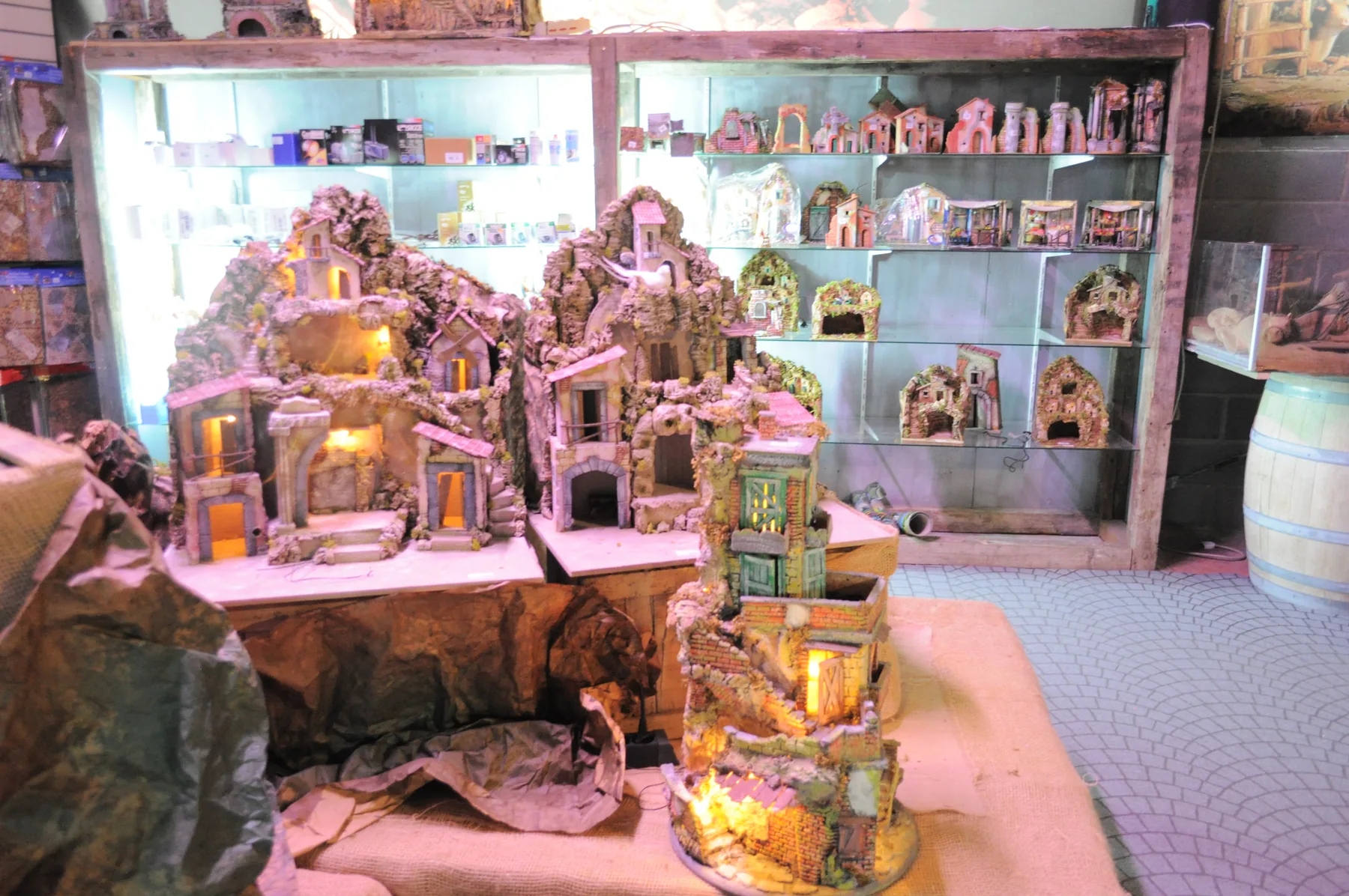 Casette da presepe in pietra illuminate su un banco, davanti agli scaffali di altri pezzi