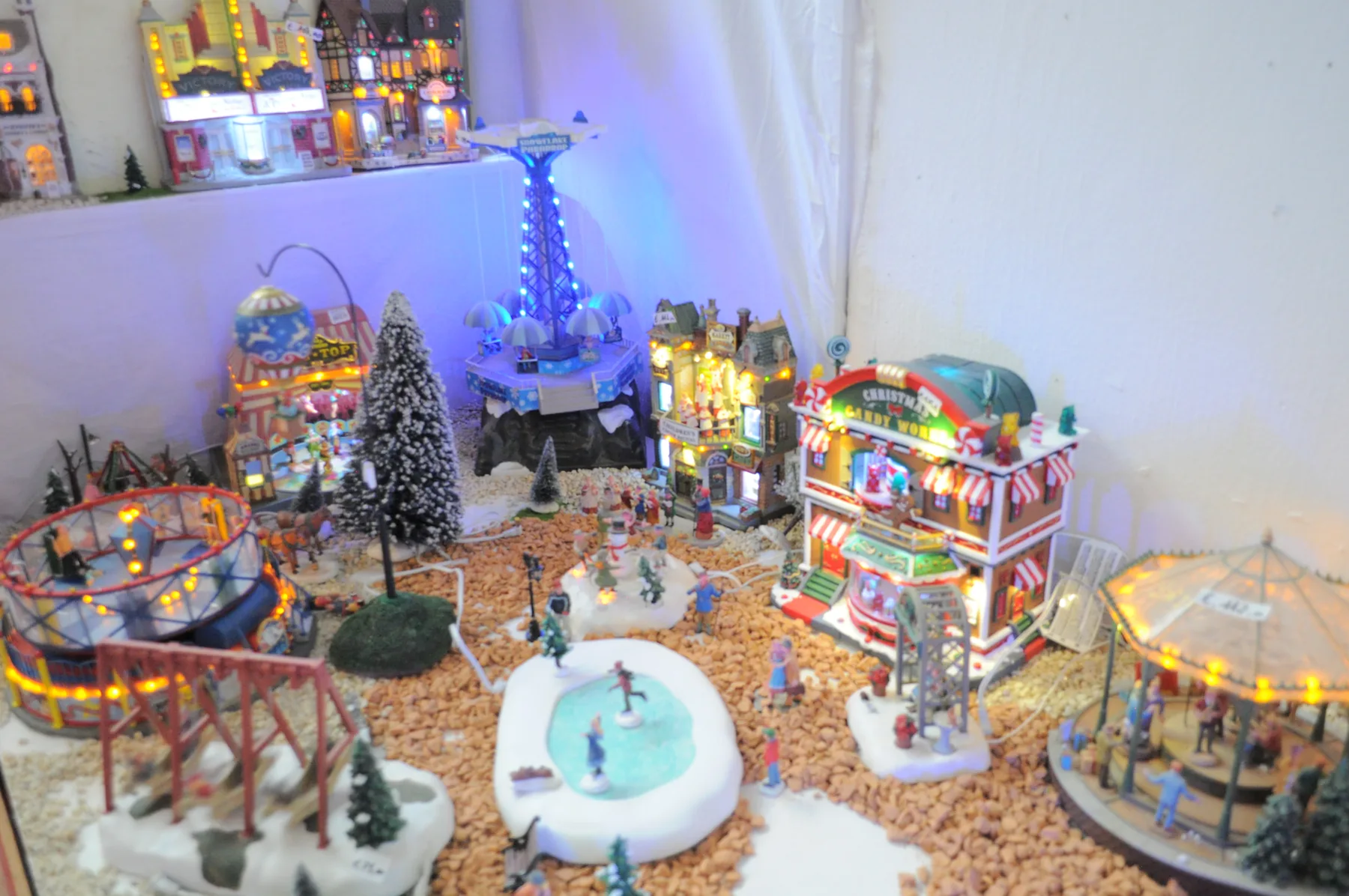 Paese in miniatura illuminato con un laghetto ghiacciato, giostre e pattinatori
