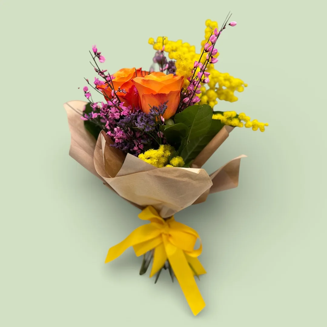 Mazzo di mimosa con tre rose arancio, limonium e ginestra fucsia, incartato