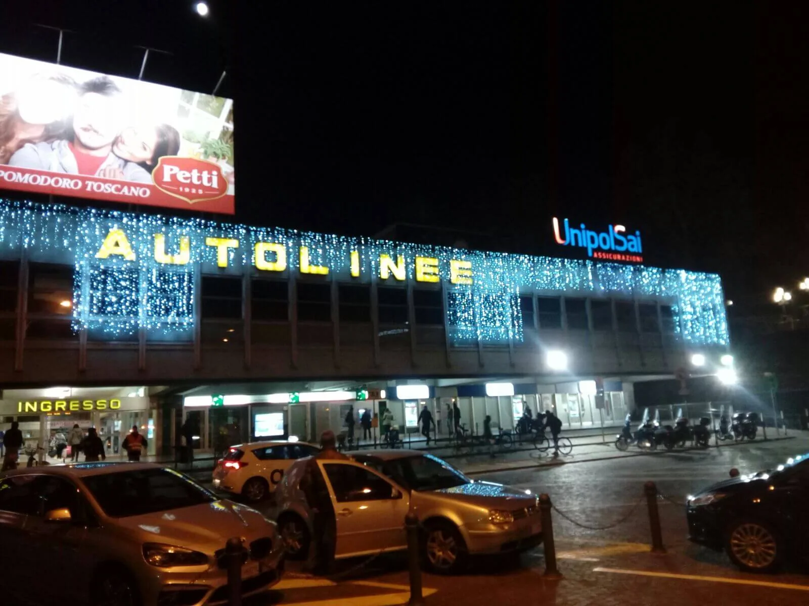 Facciata di una stazione delle autolinee di sera, con la scritta e il bordo del tetto coperti di luci bianche