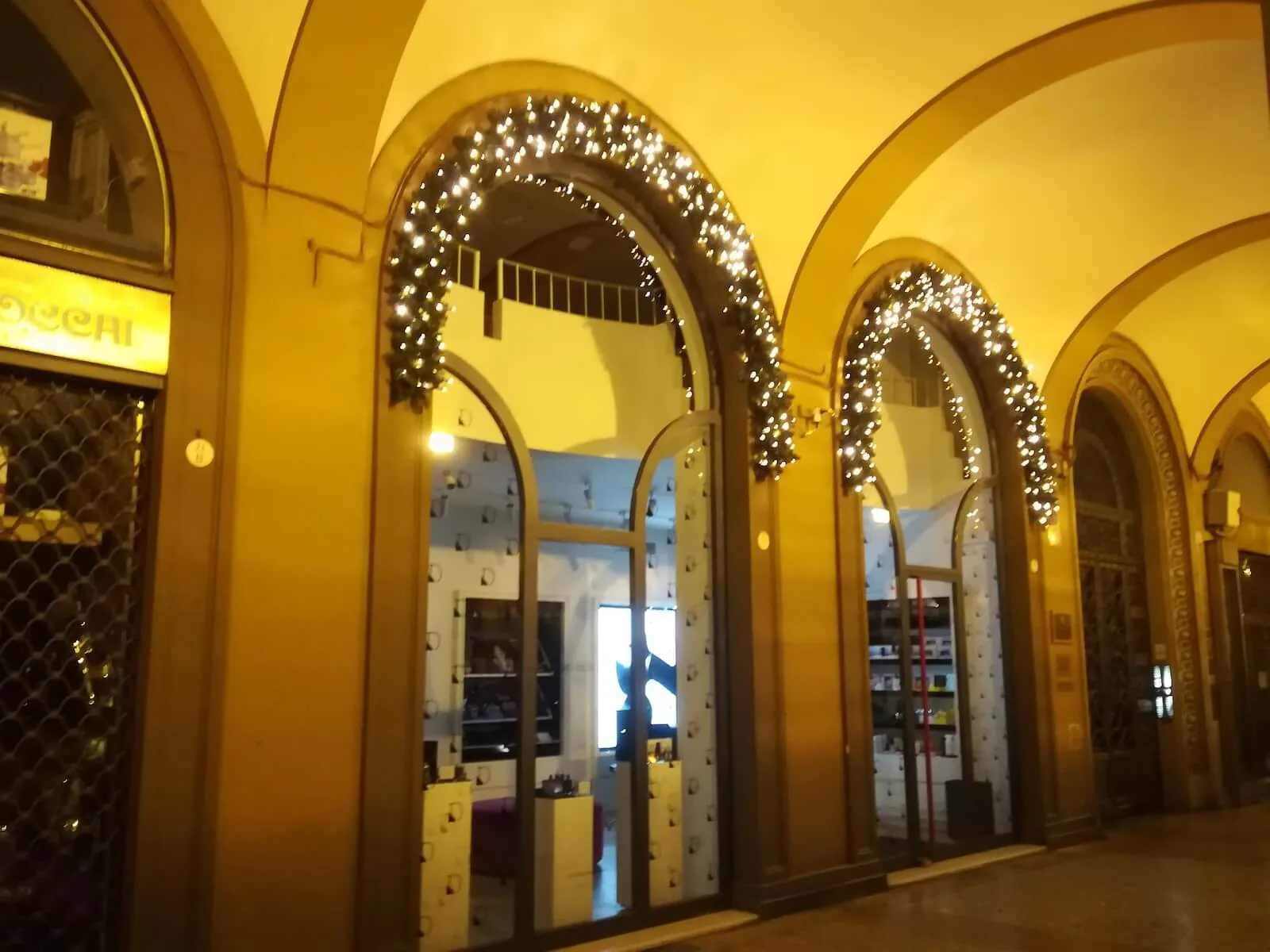 Portico ad archi con le ghirlande di luci che seguono le curve, davanti alle vetrine dei negozi
