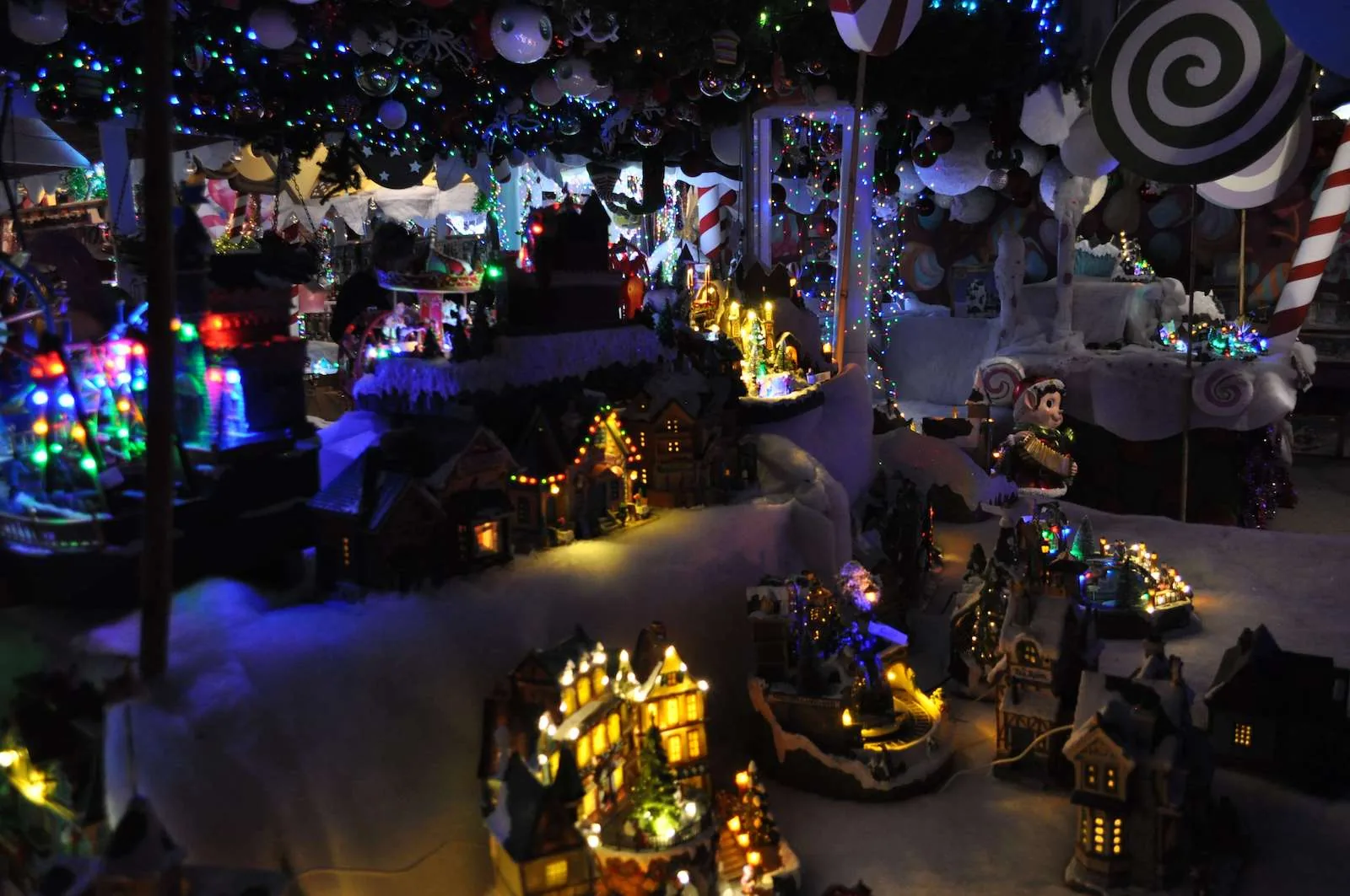 Villaggio in miniatura con casette illuminate sulla neve, sotto un soffitto di luci colorate