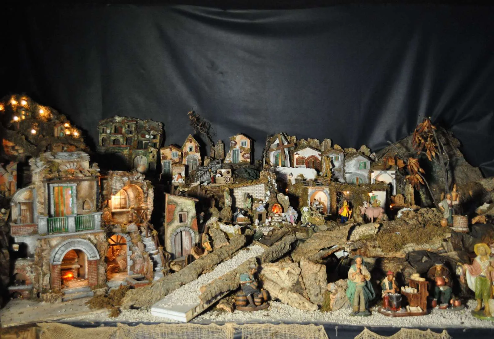 Presepe napoletano con case di roccia, ponti e statuine, su un fondale scuro