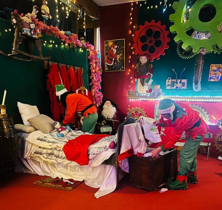 Due elfi al lavoro nella camera di Babbo Natale, fra il letto, un baule e le pareti con gli ingranaggi