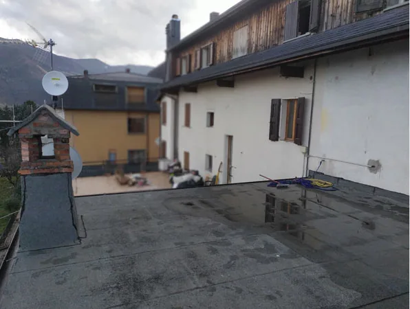 Prima: il terrazzo scoperto, con la copertura piana in guaina bagnata, un comignolo in mattoni e le case di fronte