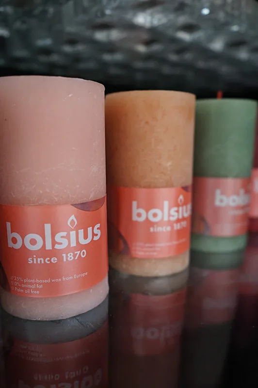 Candele a colonna rosa, arancio e verde salvia su un ripiano lucido