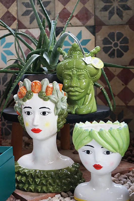 Vasi a testa di donna in ceramica colorata con piante grasse, davanti a un muro di cementine decorate