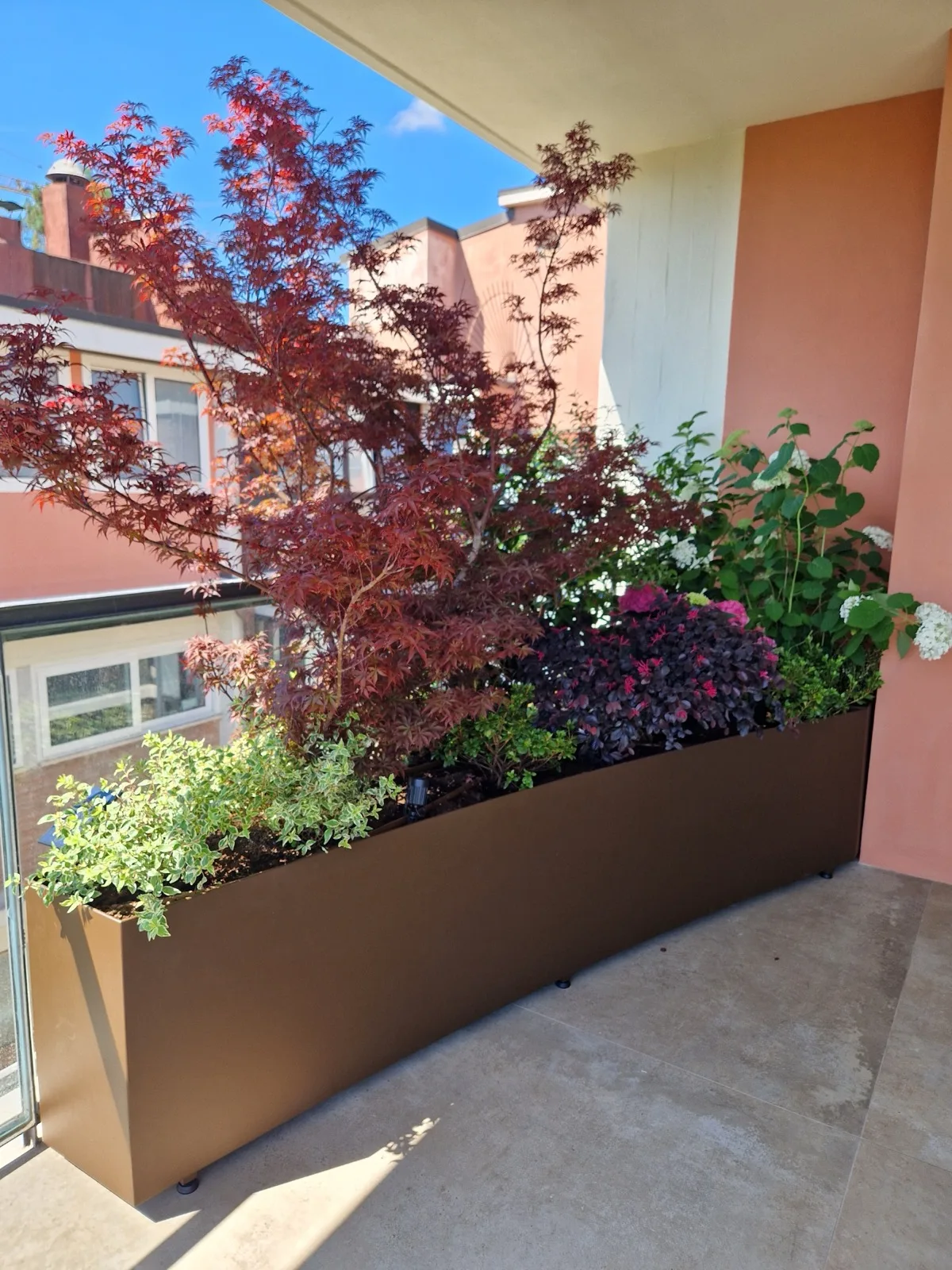 Fioriera curva in acciaio corten su un balcone, con acero rosso, ortensia bianca, heuchera scura e fioriture viola
