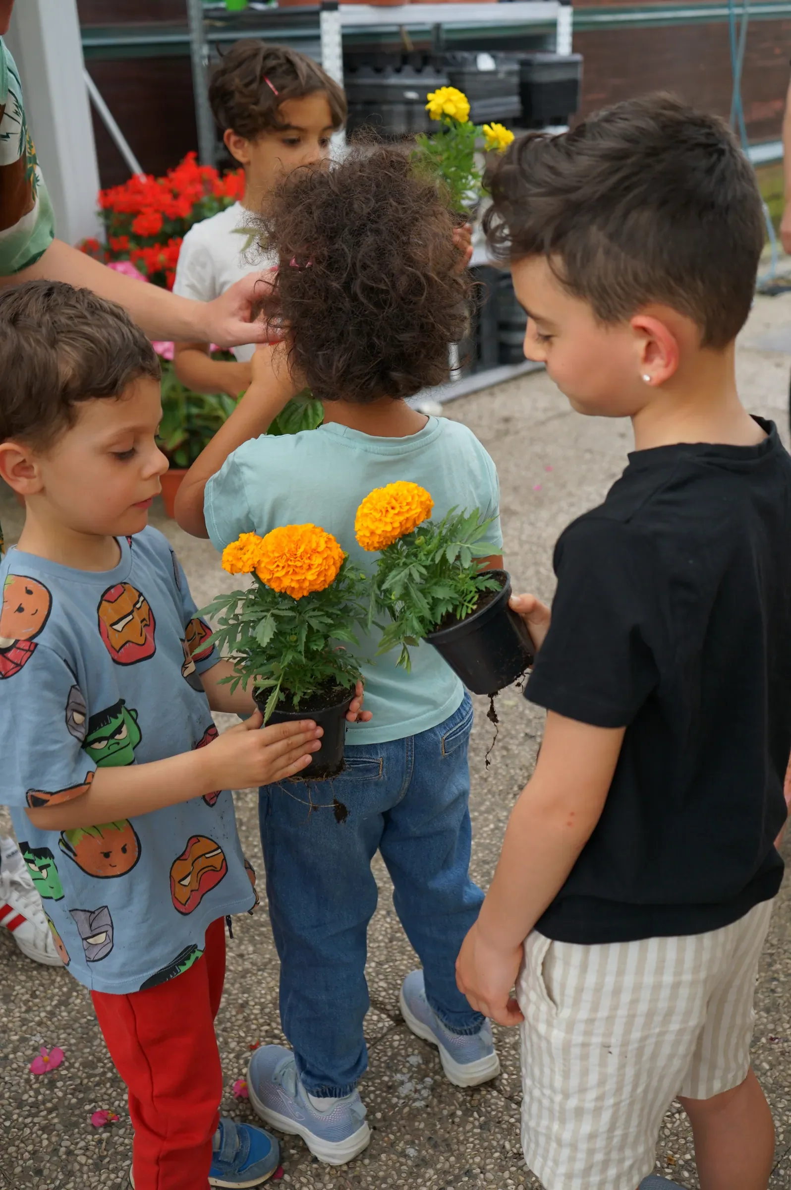 Tre bambini in piedi nel garden, due tengono in mano i vasetti con i tageti arancioni