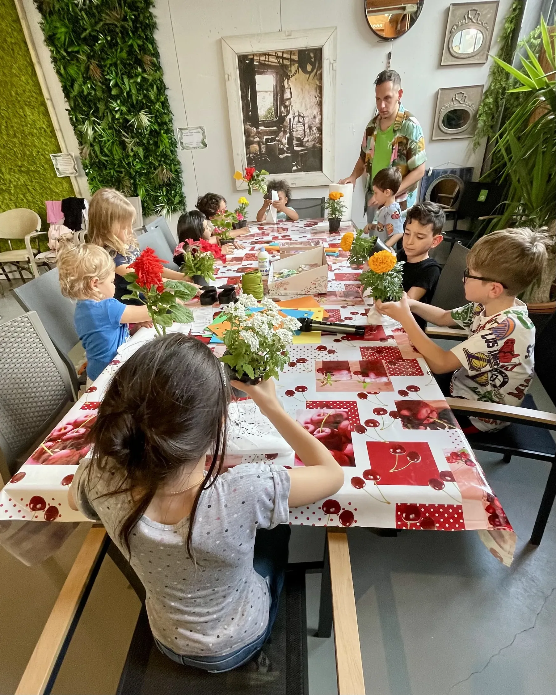 Il tavolo lungo del laboratorio visto dall'alto, con una bambina di spalle in primo piano e gli altri bambini che decorano i vasetti