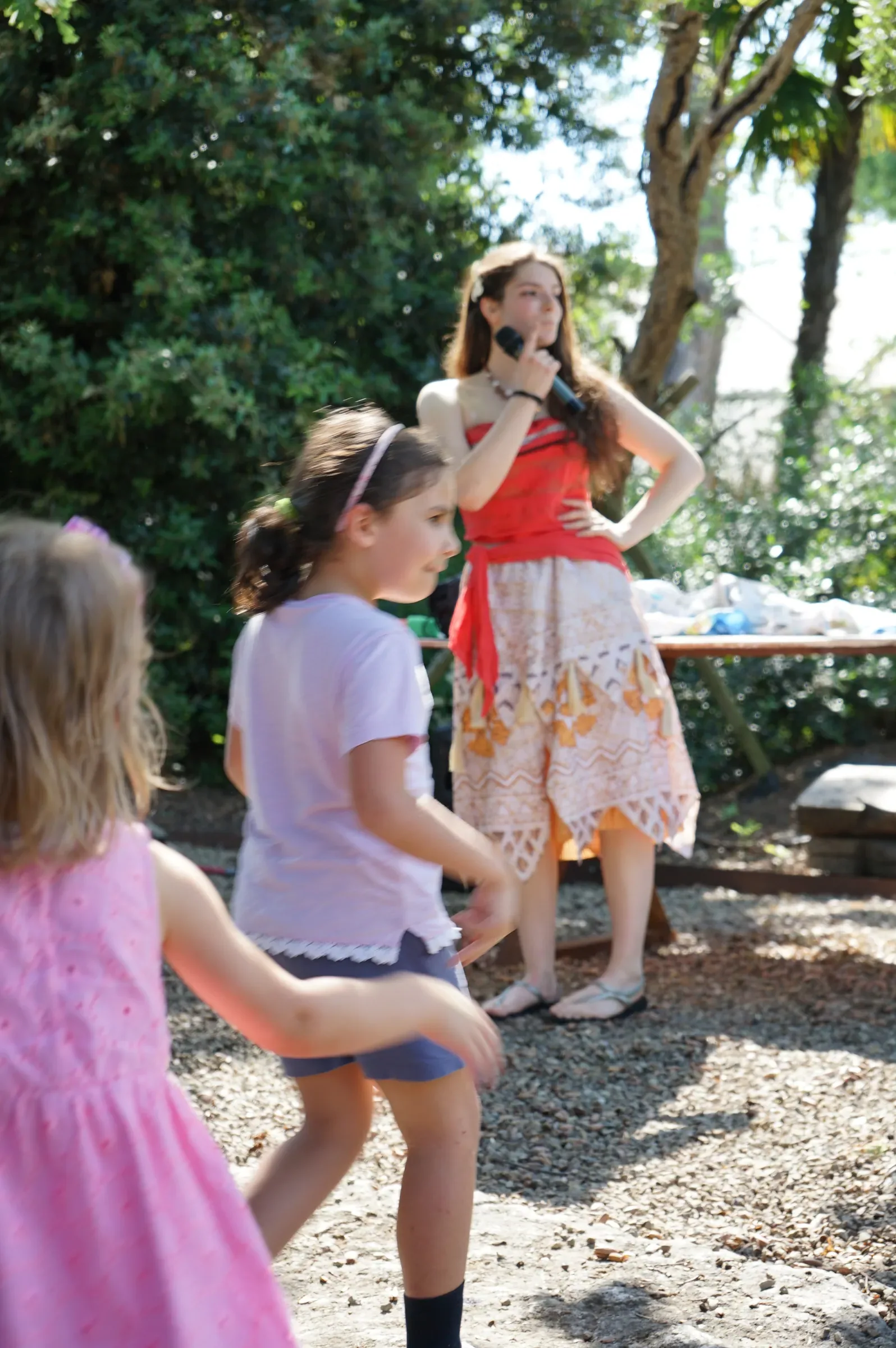 Due bambine ballano sulla ghiaia davanti a Vaiana che canta al microfono