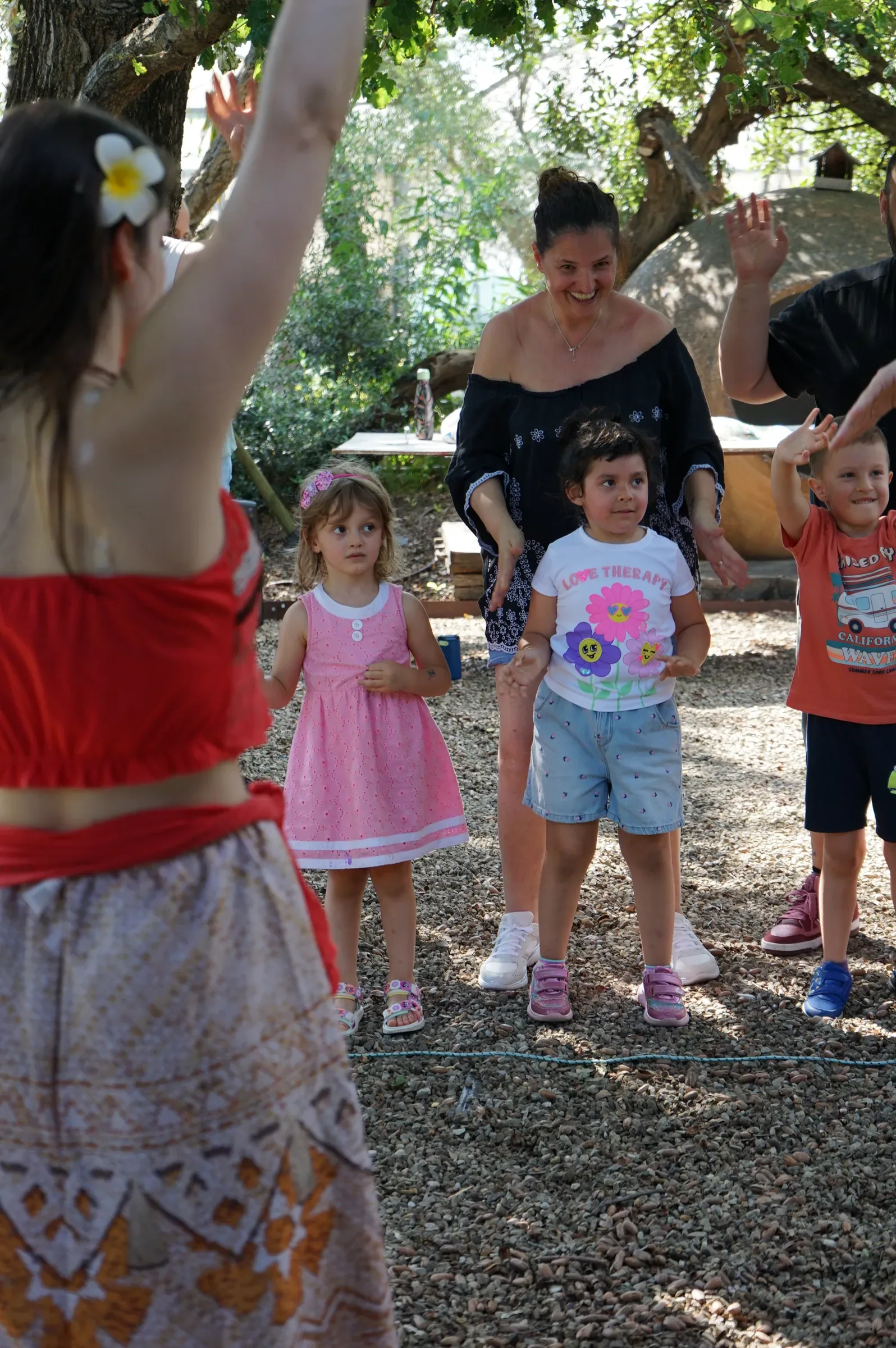 Bambini e genitori ballano a braccia alzate sotto gli alberi, con Vaiana di spalle in primo piano
