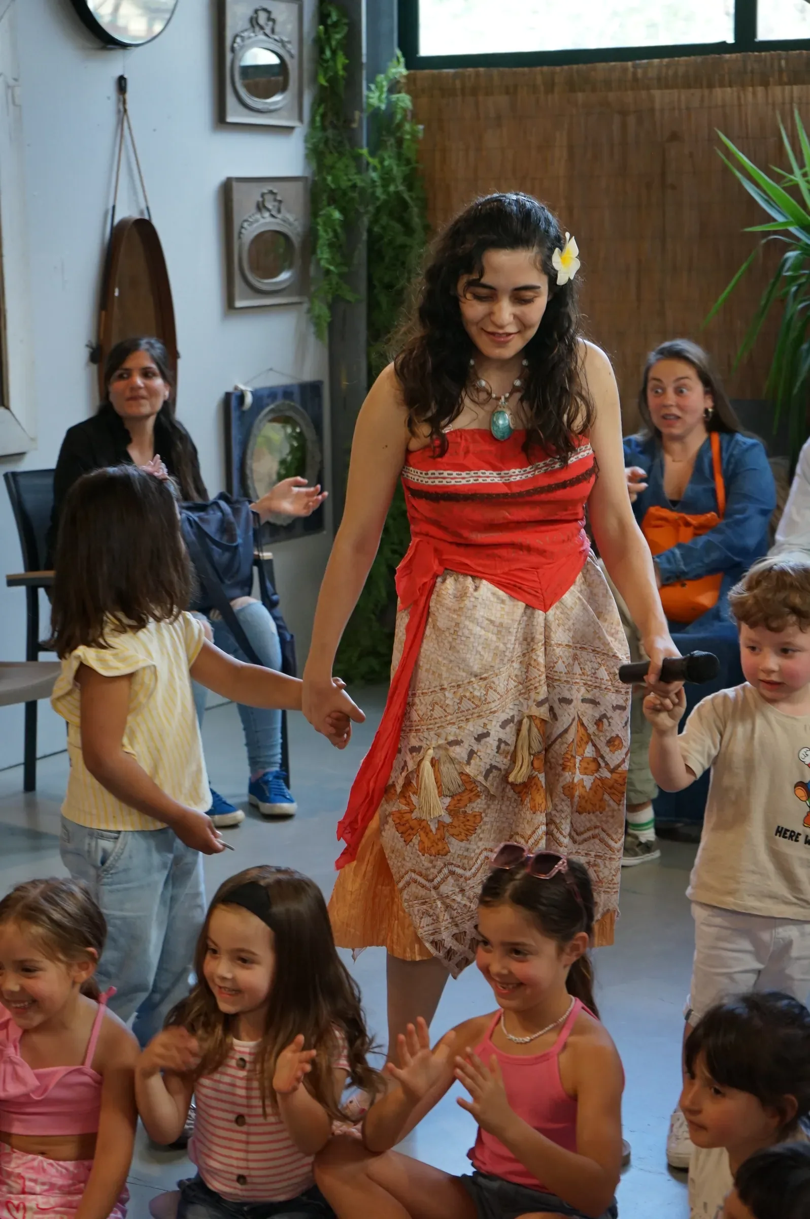 Vaiana tiene per mano due bambini, mentre le bambine sedute davanti a lei battono le mani ridendo