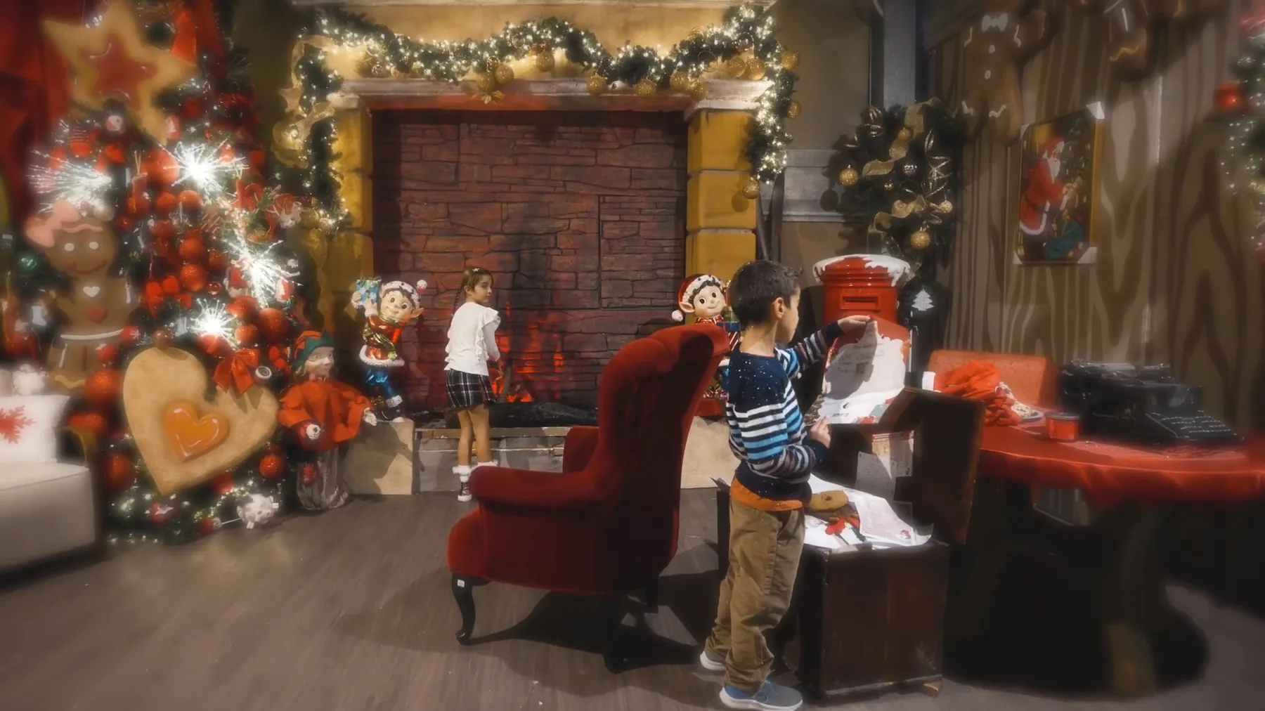 Nella casa di Babbo Natale un bambino infila una lettera nella cassetta rossa, fra la poltrona di velluto, il camino e l'albero addobbato