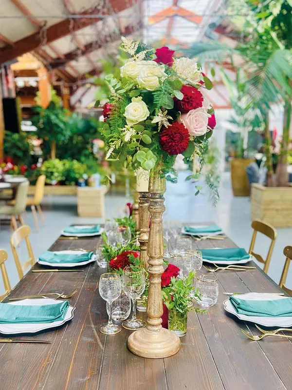 Tavolo di legno con candelieri dorati, rose rosse e bianche e tovaglioli verde acqua, in serra