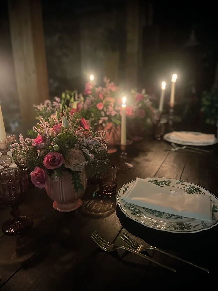 Candele accese e composizioni di rose rosa accanto ai piatti a decoro verde, di sera