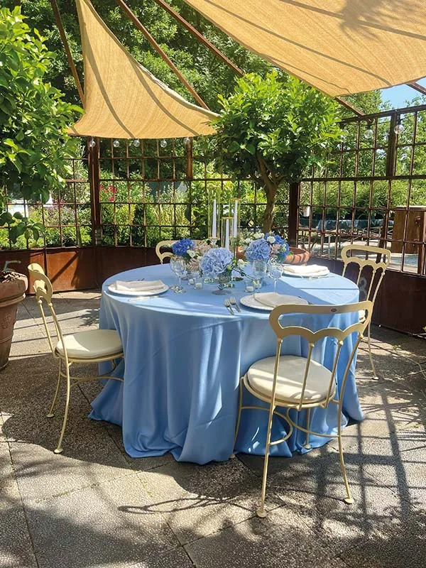 La tavola azzurra di giorno, sotto la tenda color sabbia fra gli alberi