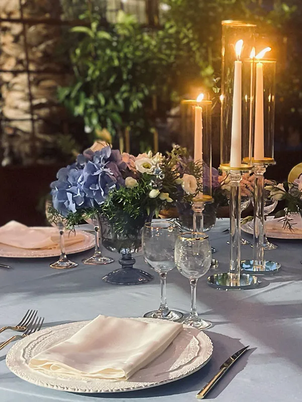 Candelabri alti e ortensie azzurre accanto ai piatti bianchi, di sera