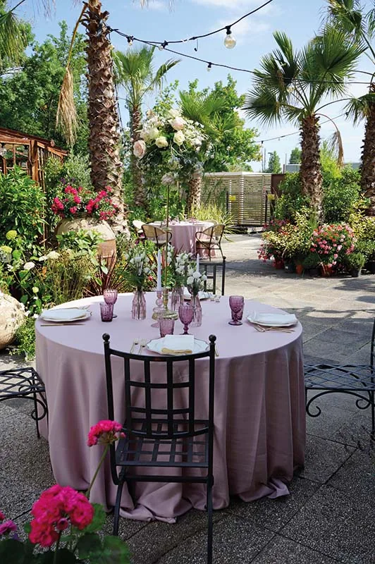 Tavola rosa con sedie in ferro fra le palme e le lucine del giardino