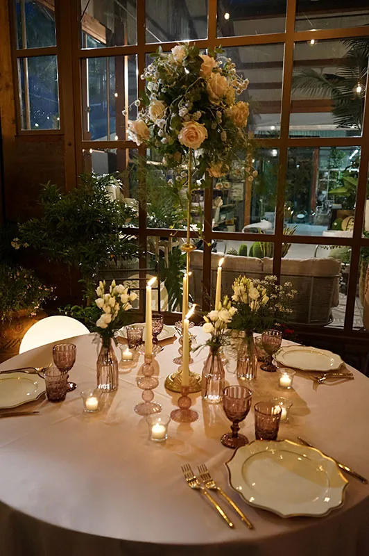 Tavola rosa di sera davanti alle vetrate della serra, con candele e rose chiare in alto